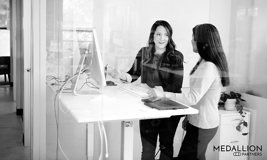 two women standing at a desk discussing recruitment and executive search and which is better for their company