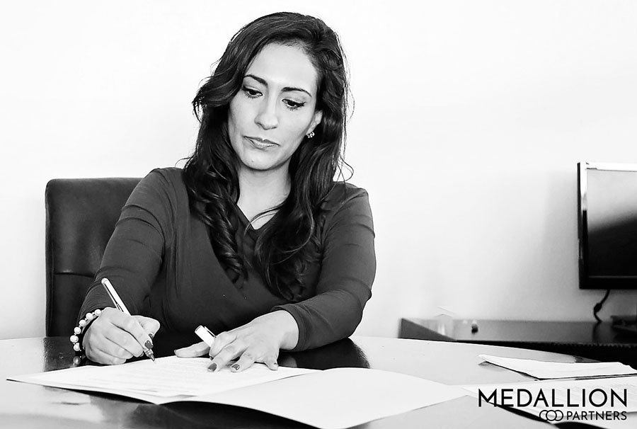 a woman writing a contract at a desk that includes the typical executive search firm fee